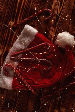 Tahta masa manzaralı çelenkler arasında kırmızı Noel şapkalı baston şekerler. Noel havası