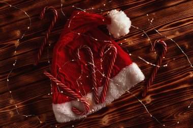 Tahta masa manzaralı çelenkler arasında kırmızı Noel şapkalı baston şekerler. Noel havası
