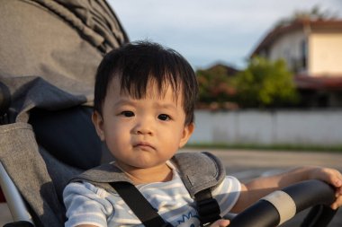 Mutlu ve şirin Asyalı bir çocuğun portresi. Bebek arabasının üzerinde akşam vakti oturuyor.
