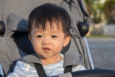 Mutlu ve şirin Asyalı bir çocuğun portresi. Bebek arabasının üzerinde akşam vakti oturuyor.