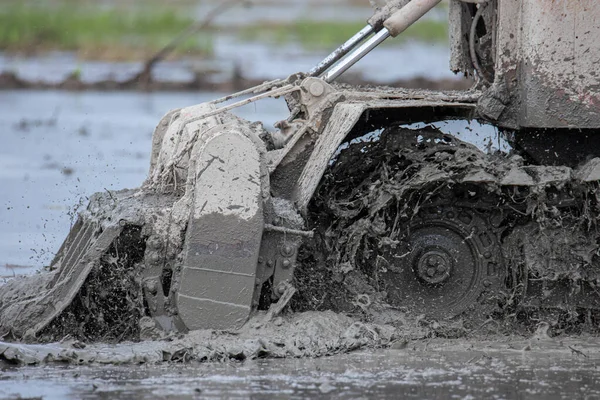 Yakından çekilen traktör tarlada yarıklar açıyor ve kesiyor. Traktör köydeki kara toprak tarlasında çalışıyor.