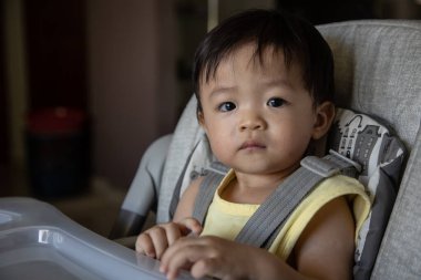 Sevimli, neşeli ve mutlu 1 yaşında Çinli bir çocuk bebek koltuğunda otururken yemek yiyor.
