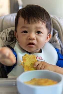 Sevimli, neşeli ve mutlu 1 yaşında Çinli bir çocuk bebek koltuğunda otururken yemek yiyor.