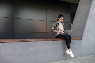 Ön manzara. Sokakta dizüstü bilgisayarı olan gömlekli bir kız çalışıyor. Uzaktan kumanda. Çevrimiçi video görüşmeleri yapıyorum. Serbest kız..