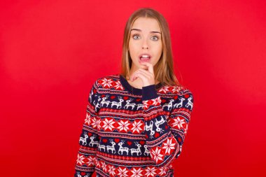 Şaşkın genç Kafkas kız yılbaşı süveteri giyerek şaşkınlıktan ağzı açılır ve ani haberlere tepki verir..