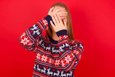 Kafkasyalı genç bir kız Noel süveteri giyiyor gözleri ve ağzı kapalı, şaşırmış ve şok olmuş. Duyguları gizlemek.