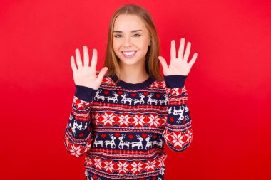 Kafkasyalı genç bir kız Noel süveteri giyer ve parmaklarını on numarayla göstererek gülümserken kendinden emin ve mutlu..
