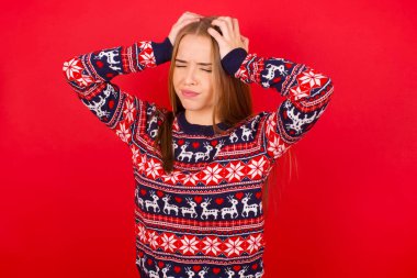 Kırmızı arka planda Noel süveteri giyen genç beyaz kız aşırı çalışmaktan dolayı şiddetli baş ağrısı ve stresten muzdarip. Depresyon ve acı kavramı.