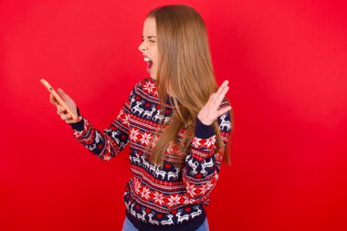 Kırmızı arka planda Noel süveteri giyen kızgın genç beyaz kız telefonda bağırıyor, bir çalışanla tartışıyor. İşte sorunlar var..
