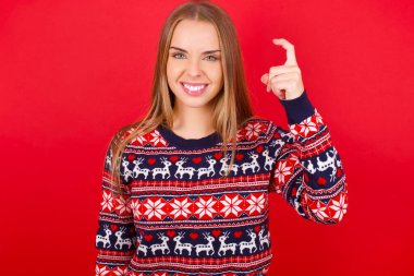 Kırmızı arka planda Noel süveteri giyen genç beyaz kız Çince işaret dilinde dokuz numara Jiu 'yu işaret ediyor.