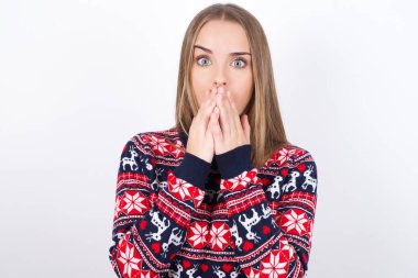 Beyaz arka planda Noel süveteri giyen beyaz tenli genç bir kız elleri ağızda, gözleri inançsızlıkla dolu, çalışmaktan kafası karışmış bir şekilde bakıyor.