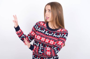 Beyaz arka planda Noel süveteri giyen Kafkasyalı genç kız ellerini boş alana uzatıyor ve yakına gelmemesini istiyor.