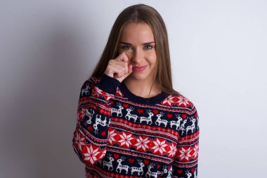 Beyaz arka planda Noel süveteri giyen üzgün genç beyaz kız gözyaşlarını kasvetli bir ifadeyle tutuyordu. Olumsuz duygu