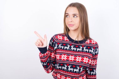 Beyaz arka plan noktalarında Noel süveteri giyen beyaz tenli genç beyaz bir kız fotokopi alanında reklamlar yapıyor..