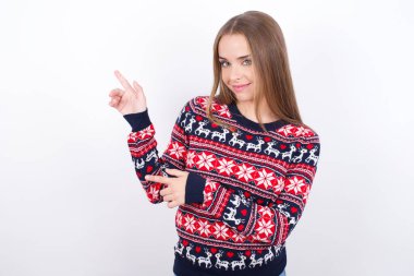Beyaz arka planda Noel süveteri giyen beyaz saçlı genç beyaz bir kız.
