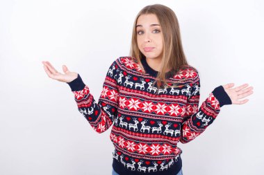 Dikkatsiz, çekici, beyaz arka planda Noel süveteri giyen, omuzlarını silkeleyen beyaz beyaz bir kız..