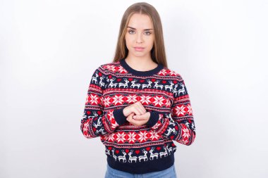 Beyaz arkaplanda Noel süveteri giyen neşeli, kendinden emin beyaz bir kızın fotoğrafı.