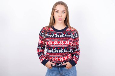 Beyaz arka planda Noel süveteri giyen hoş, komik, beyaz bir kızın portresi.