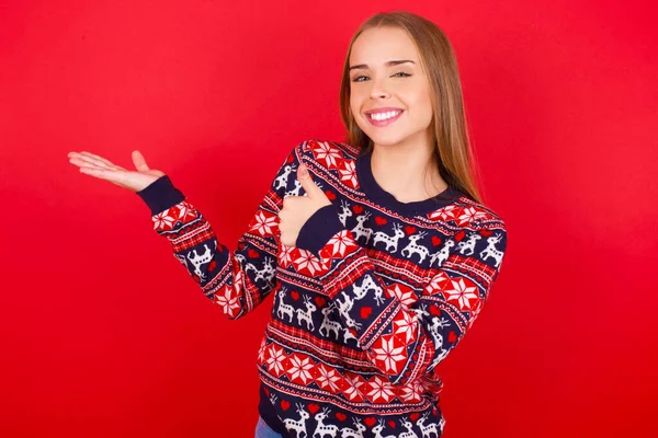 年轻的高加索女孩穿着圣诞毛衣 手牵着手 竖起大拇指 做着一个正常的动作 面带微笑 快乐而快乐 — 图库照片