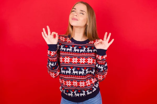 穿着圣诞毛衣的年轻的高加索女孩放松了 闭上双眼微笑着 用手指做冥想动作 瑜伽概念 — 图库照片