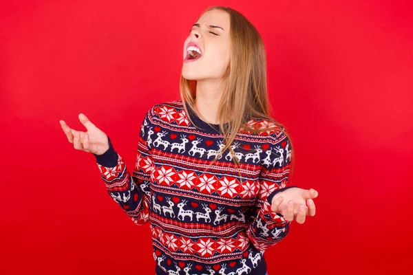 年轻的高加索女孩穿着圣诞毛衣 疯狂地大喊大叫 带着咄咄逼人的表情和手臂 沮丧的概念 — 图库照片