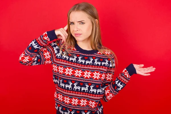 年轻的高加索女孩穿着红色背景的圣诞毛衣 对开放的手掌展示复制空间和指尖指向额头感到困惑和恼怒 你想想吧 — 图库照片