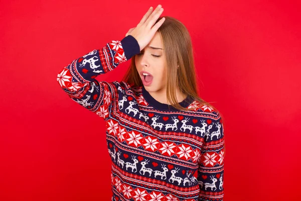 年轻的高加索女孩穿着红色背景的圣诞毛衣 手头上的错误让人吃惊 记住错误 记性差 — 图库照片