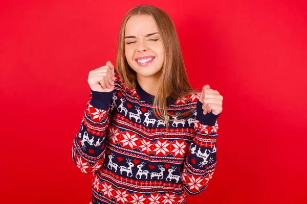 Młoda Biała Dziewczyna Świątecznych Swetrach Czerwonym Tle Jest Podekscytowana Sukcesem — Zdjęcie stockowe