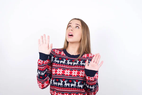 年轻的高加索女孩穿着白色背景的圣诞羊毛衫 手心前倾 在天花板上惊恐地看着上方 竭力保护自己不受看不见的危险的伤害 张开嘴 — 图库照片