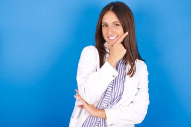 Güzel genç bir kadın kameraya bakıyor kollarını kavuşturup gülümsüyor ve elleri çenesinde yükseliyor. Olumlu düşünüyorum..