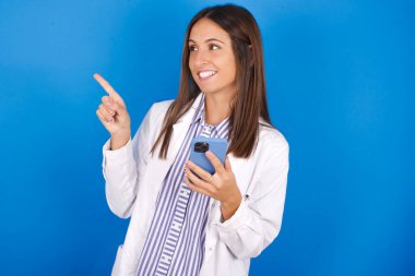 Vay canına! Heyecanlı güzel Latin kadın cep telefonunu açık el hareketleriyle gösteriyor.