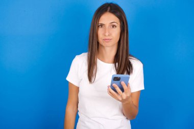 Memnun olmayan genç bir kadın mobil yazılım uygulaması kullanıyor ve internette bilgi sörfü yapıyor, modern mobil elini tutuyor.