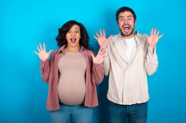 İyimser genç çift mavi arka planda bebek beklerken sevinçten avuçlarını kaldırıyor, birinden müthiş bir hediye almaktan mutlu oluyor, yüksek sesle bağırıyor, heyecanlı bir manken gibi çığlık atıyor..