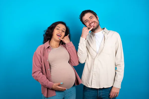 Jovem Casal Esperando Bebê Contra Fundo Azul Sorrindo Fazendo Gesto — Fotografia de Stock