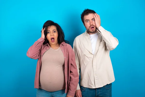 Peinliches Junges Paar Erwartet Baby Vor Blauem Hintergrund Mit Schockiertem — Stockfoto
