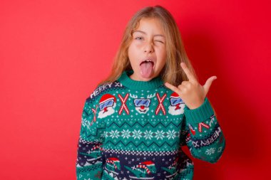 Kırmızı arka planda örgü örülü süveter giyen komik esmer bir kızın portresi. Dil boynuzlarını gösteriyor, orkestra konserinde olmanın heyecanını anlatıyor..