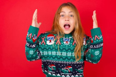 Kırmızı arka planda örgü süveter giyen neşeli, şanslı esmer kız tezahürat yapıyor, başarıyı kutluyor, yumruklarını sıkarak evet diye bağırıyor.