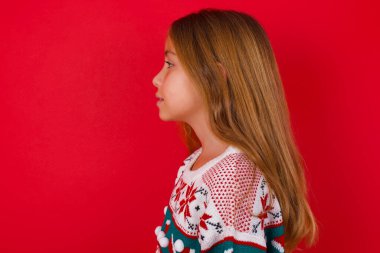 Kırmızı arka planda örgü süveter giyen güzel esmer bir kızın profil portresi boş, dişlek bir gülümseme.