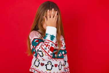 Kırmızı arka planda örülü süveter giyen esmer kız. Ağlarken suratını ellerle kapatan üzgün bir yüz ifadesi var. Depresyon kavramı.