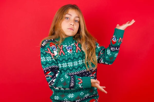 Brunette Kid Girl Knitted Sweater Christmas Red Background Pointing Aside — Stock Photo, Image