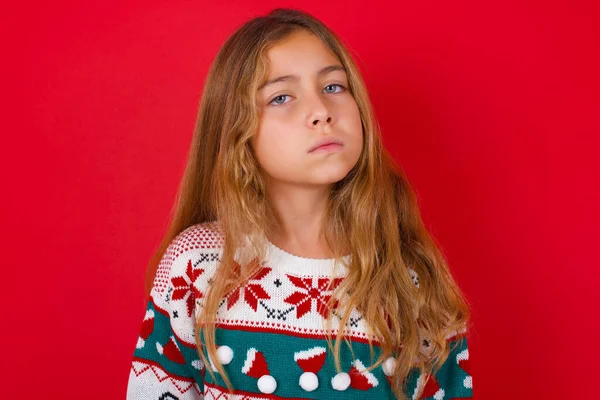 赤い背景の眉の顔の上にニットセーターのクリスマスで不満ブルネットの子供の女の子は不幸ないくつかの問題を抱えている感じている 否定的な感情や感情の概念 — ストック写真