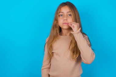 Esmer kız mavi arka plan ağzı üzerine süveter giyiyor ve dudakları parmaklarıyla fermuar gibi kapalı. Gizli ve sessiz, tabu konuşması.