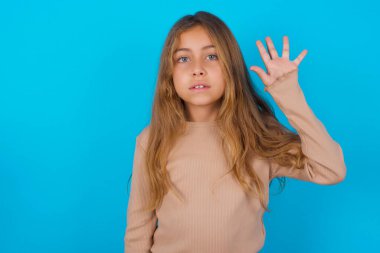 Mavi arka planda süveter giyen esmer kız beş numarayı gösterip işaret ederken kendinden emin ve mutlu gülümsüyor..