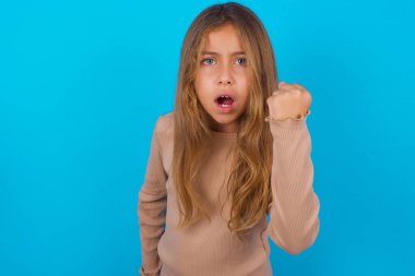 brunette kid girl wearing sweater over blue background angry and mad raising fist frustrated and furious while shouting with anger. Rage and aggressive concept. clipart