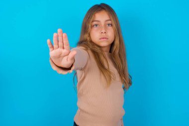 Mavi arka planda süveter giyen esmer kız avuç içiyle şarkı söylemeyi kesiyor. Yüzünde olumsuz ve ciddi bir jest olan uyarı ifadesi.