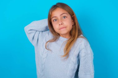 Mavi arka planda mavi örgü süveter giyen esmer kız kafası karışmış ve bir şeyi merak ediyor. El ele tutuşmak, şüpheyle emin olmak. Düşünceli kavram.