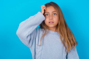 Utangaç, esmer kız mavi örgü süveter giyen, şaşkın bir ifadeyle şaşırmış, kapalı mekanda şaşkın poz veren kız.
