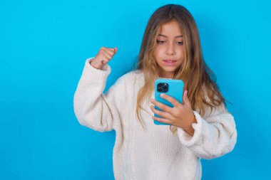 Mavi arka plan üzerine beyaz örülü süveter giyen esmer kız el ele tutuşmuş ve iyi haberleri okuduktan sonra heyecanla yumruğunu kaldırıyor..