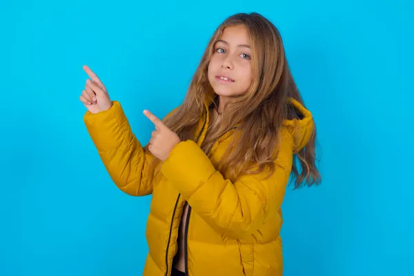 Брюнетка Дівчинка Жовтій Куртці Синьому Фоні Вказує Порожній Простір Пальця — стокове фото