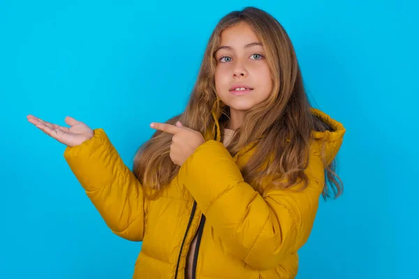 Brunetka Dziecko Dziewczyna Noszenie Żółty Kurtka Niebieskie Tło Wskazując Trzymając — Zdjęcie stockowe